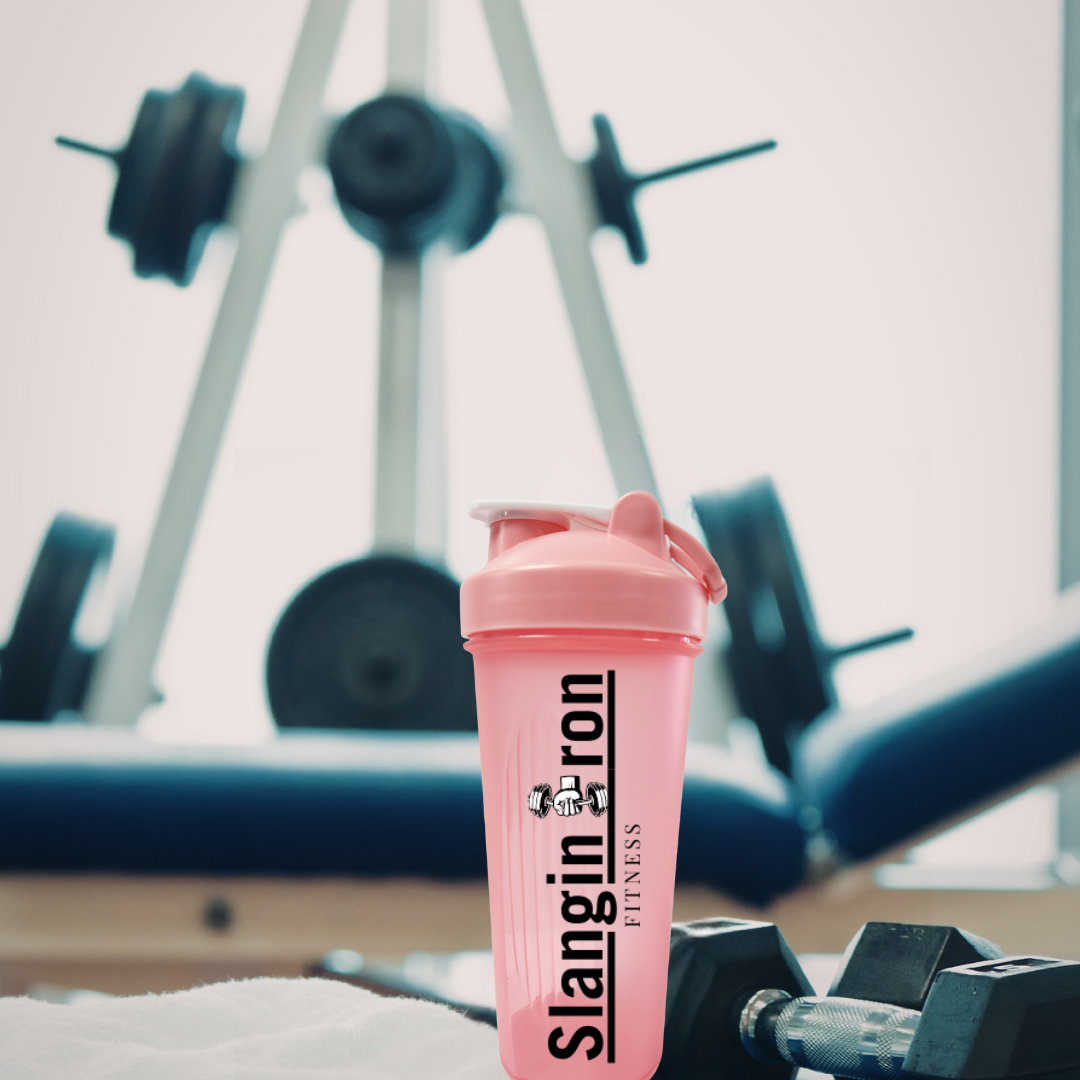 Pink shaker bottle with 'Slangin Iron Fitness' branding in a gym setting